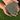 Hand holding a clump of green sand or gravel against a grassy background