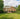 Brick house with a green lawn and trees under a cloudy sky